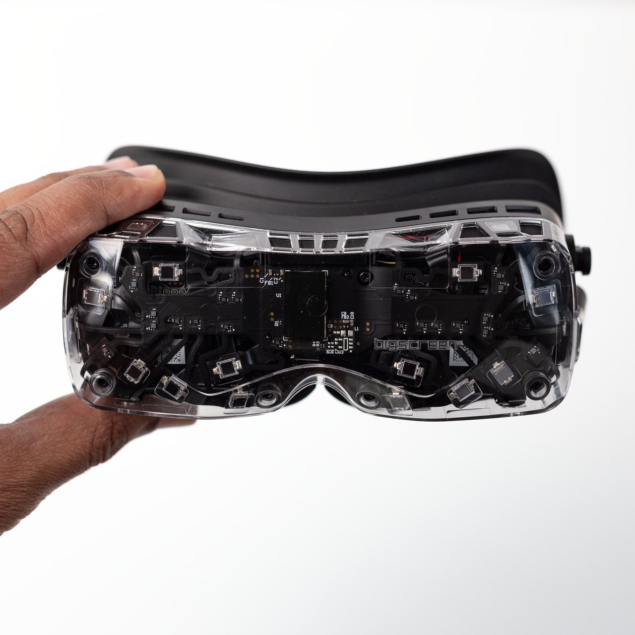Bigscreen Beyond 2 in its clear shell held in one hand, showing the tracking sensors behind the faceplate