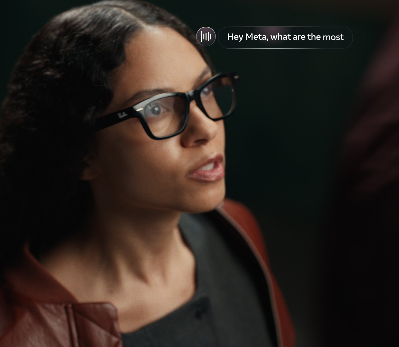 A woman wearing black rectangular Ray-Ban frames speaks a voice request, shown as an on-screen Hey Meta prompt beside her head