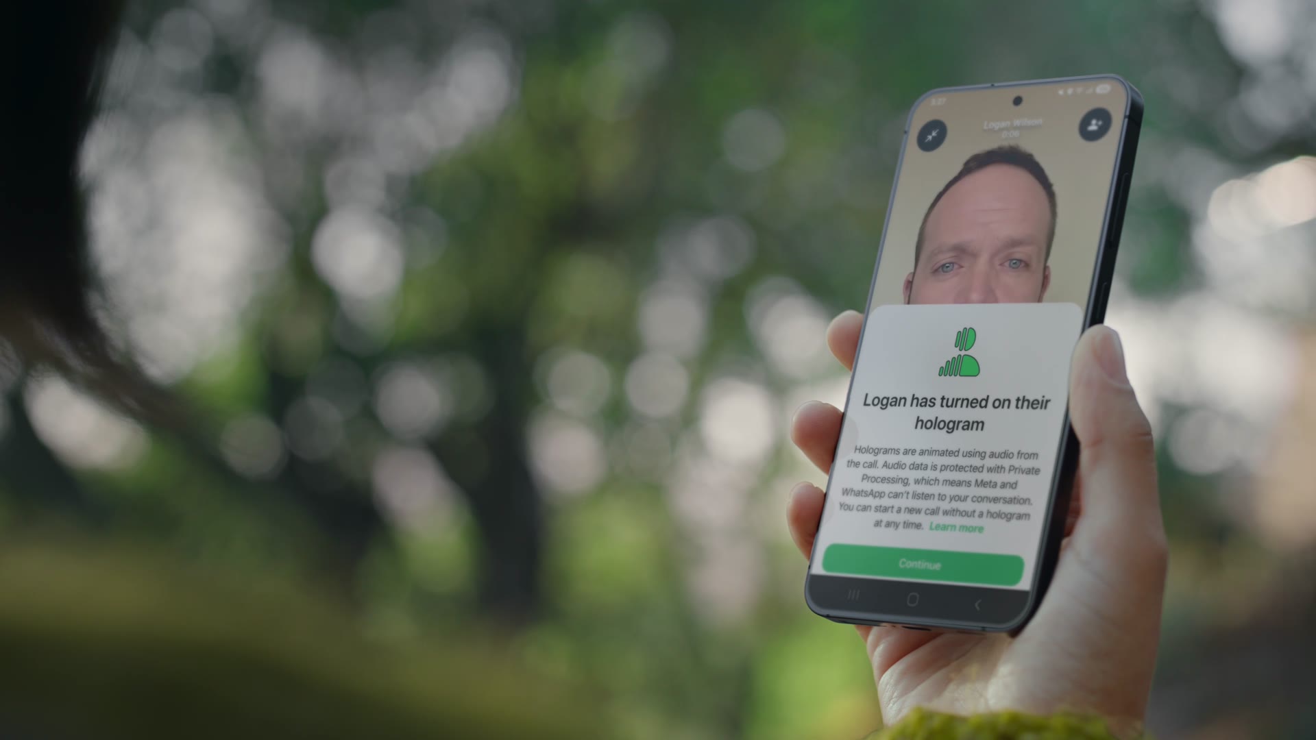 A hand holding a phone outdoors showing a WhatsApp call with a man's hologram avatar and a notice card reading Logan has turned on their hologram, explaining that holograms are animated using audio from the call