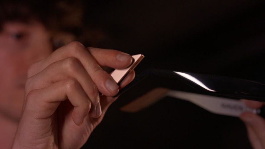 A hand sliding a Raven Wings hot-swappable battery module into the temple arm of the Raven Prism glasses