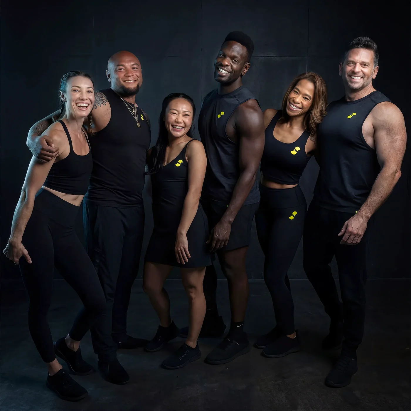 The six returning Supernatural coaches photographed together in Supernatural-branded workout gear against a dark studio backdrop